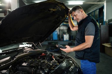 Auto mechanic using diagnostic work tool while checking car engine in a workshop. 
