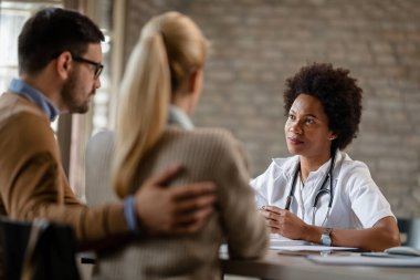 African American general practitioner having consultations with a couple at medical clinic. 