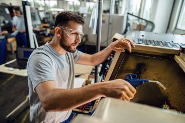 Factory worker using CNC machine while working in industrial plant.