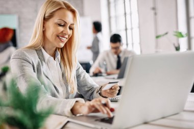 Happy businesswoman using laptop and credit card for shopping online in the office. 