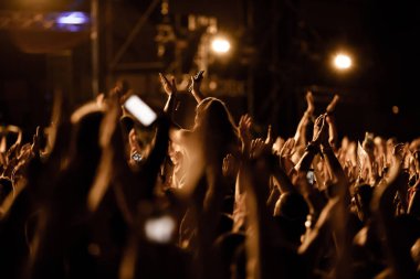 Excited crowd of people cheering on music festival and clapping with arms raised. 
