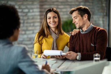 Happy mid adult couple reading documents and communicating with financial advisor in the office. Focus is on happy woman. 