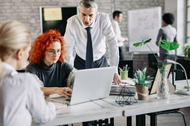 Business colleagues working on computer during a meeting in the office. Focus is on young redhead businesswoman.