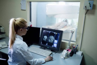 Radiologist analyzing brain MRI scan results of a patient on computer monitor in control room. 
