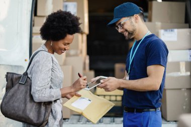Happy black woman using digitized pen and signing on touchpad while getting her package delivered, 