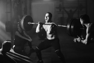 Black and white photo of sportsman making an effort and screaming while weightlifting on cross training in a gym. 