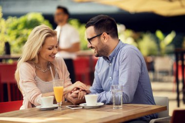 Happy man  holding hands with his girlfriend and talking to her while being on a date in a cafe. 