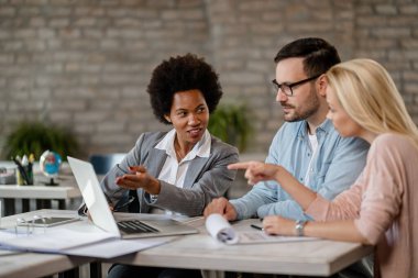 Black female insurance agent using computer with a couple during consultations in the office.
