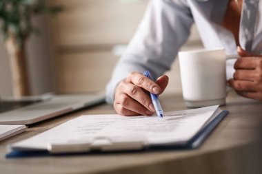 Close up of unrecognizable entrepreneur going through business reports while drinking coffee in the office. 