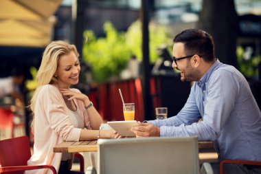Cheerful man relaxing with his girlfriend in a cafe and showing her something on a touchpad. 