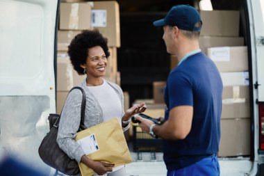 Happy black woman communicating with a courier while getting her package delivered. 