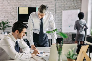 Happy businessman and his colleague going through paperwork and reading charts in financial report in the office. 