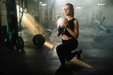 Female athlete with kettle bell practicing lunge on cross training in health club. 