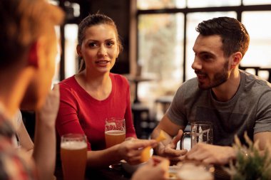 Group of young people drinking beer and eating tortilla chips while spending time together in a tavern. Focus is on young woman. 