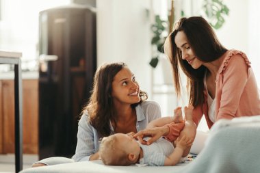 Female couple talking while playing with their baby boy at home. 