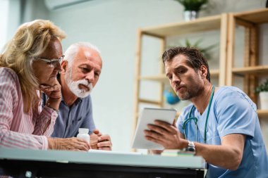 Low angle view of senior couple and their doctor using touchpad during medical appointment. 
