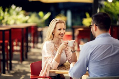 Happy woman enjoying in conversation with her boyfriend while drinking coffee in an outdoor cafe. 