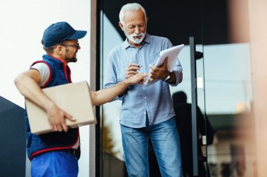 Senior man receiving home delivery while courier is pointing at place he need to sign. 