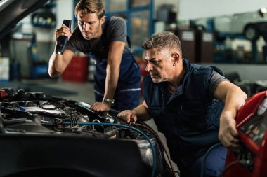 Two mechanics using compressor while working on car's air conditioning system in auto repair shop. 