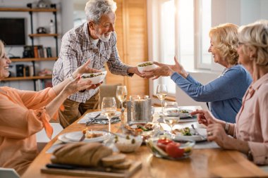 Happy senior man serving lunch to his friends at dining table. 