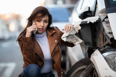 Young woman feeling distraught after a car accident and calling for roadside assistance over mobile phone. 