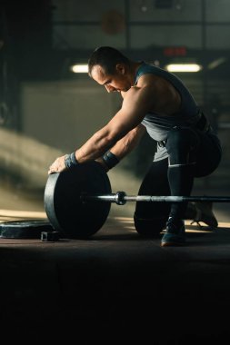 Athletic man preparing barbell for weight training in a gym. Copy space. 