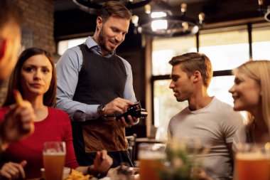 Young waiter accepting credit card payment from his guest who is paying restaurant bill. 