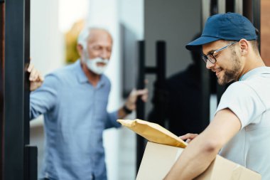 Smiling postal worker checking the label on a package while making a delivery to customer's home. 