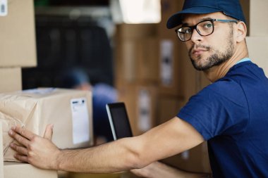 Delivery man scanning bar code on a package with a touchpad while looking at camera. 