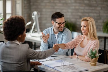 Happy woman shaking hands with financial advisor while being on a meeting with her husband in the office. 