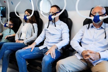 Small group of people breathing through masks while having hyperbaric oxygen therapy at clinic. Focus is on mid adult man. 
