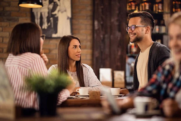 Group of friends drinking coffee and talking to each other in coffee shop. Focus is on a woman.