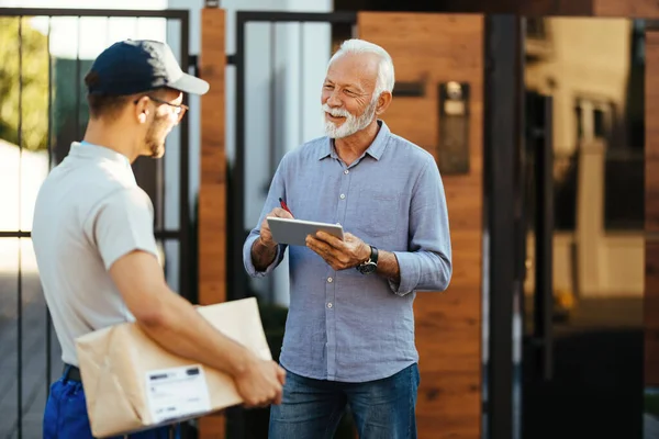 Happy Mature Man Signing Digital Tablet Delivery While Communicating Courier — Stock Photo, Image
