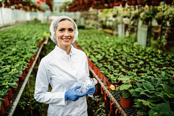 Portrait of smiling female scientist standing in a greenhouse and looking at camera.