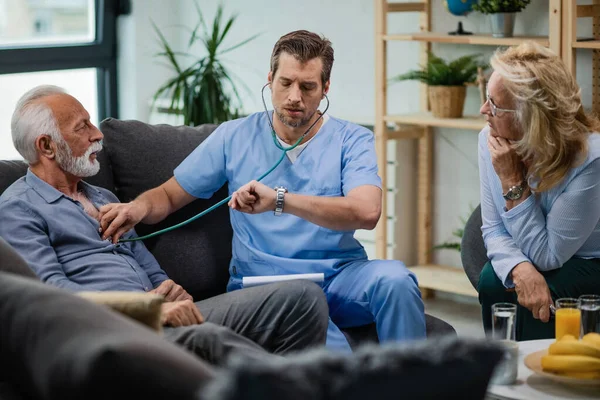 Doctor Visiting Senior Couple Home Checking His Wristwatch While Listening — Fotografia de Stock