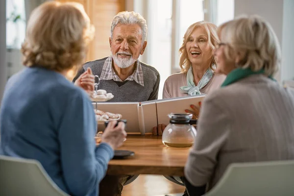 Group of happy mature people talking about their memories while gathering at home. Focus is on mature couple with photo album.