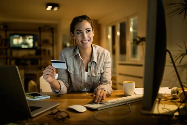 Young happy woman with credit card shopping online in the evening at home.