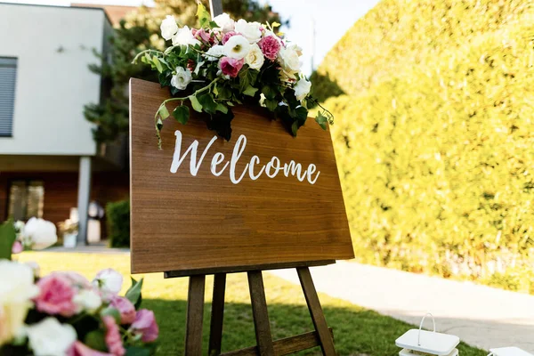 Welcome board with rose bouquet at outdoor wedding venue.