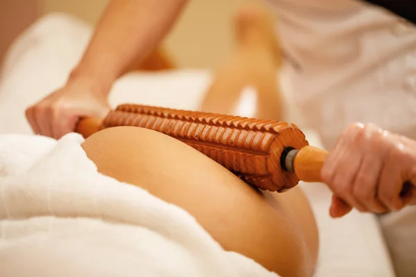 Close-up of woman getting buttocks massage with wooden rolling pin during maderotherapy at the spa. 
