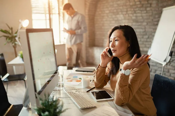 Asian Businesswoman Reading Charts Desktop Communicating Cell Phone Office — Stock Fotó