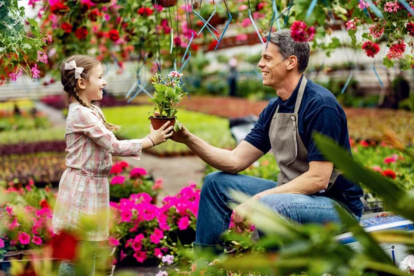 Happy father giving his small daughter potted flower while she's helping him in a garden center.