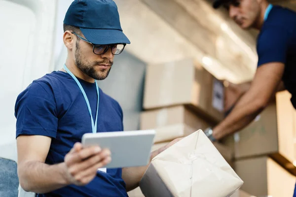 Young Delivery Man Using Touchpad While Reading Label Package — Foto Stock