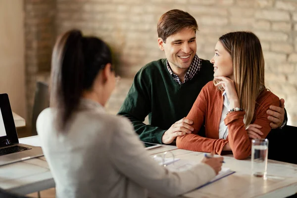 Young Smiling Couple Communicating While Being Meeting Financial Advisor — стоковое фото