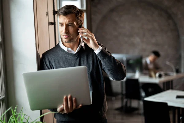 Бизнесмен Держит Ноутбук Разговаривает Мобильному Телефону Стоя Окна Офисе — стоковое фото