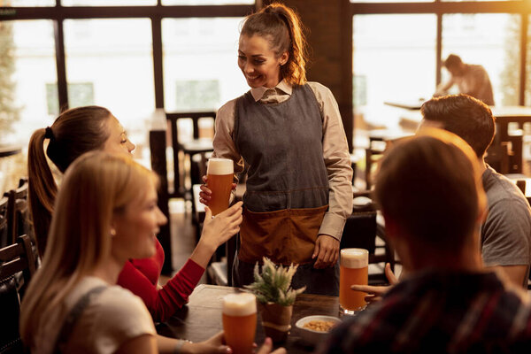 Happy waitress serving beer to group of young people in a pub. 