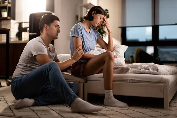 Young displeased woman ignoring her boyfriend who is trying to apologize after a quarrel in the bedroom.