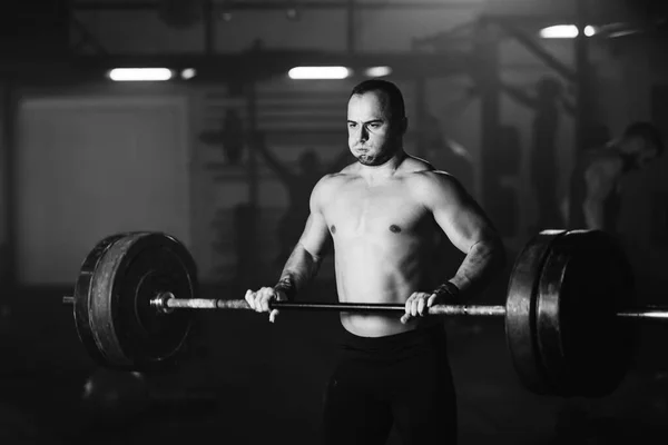 Black and white photo of shirtless sportsman having weight training with a barbell in health club.