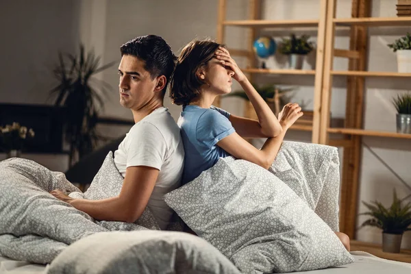 Young sad couple ignoring each other while sitting back to back on the bed.