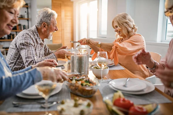 Happy mature friends having fun while sharing food during lunch time at dining table. Focus is on mature couple.