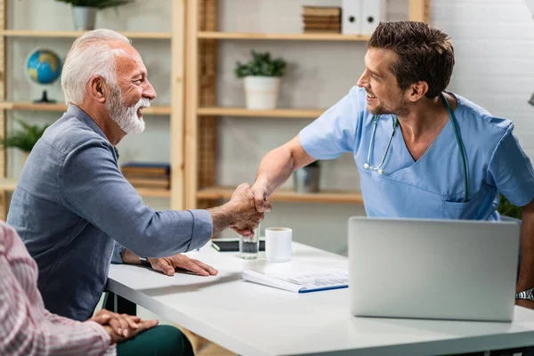 Happy doctor and mature man greeting and shaking hands during medical consultations. 